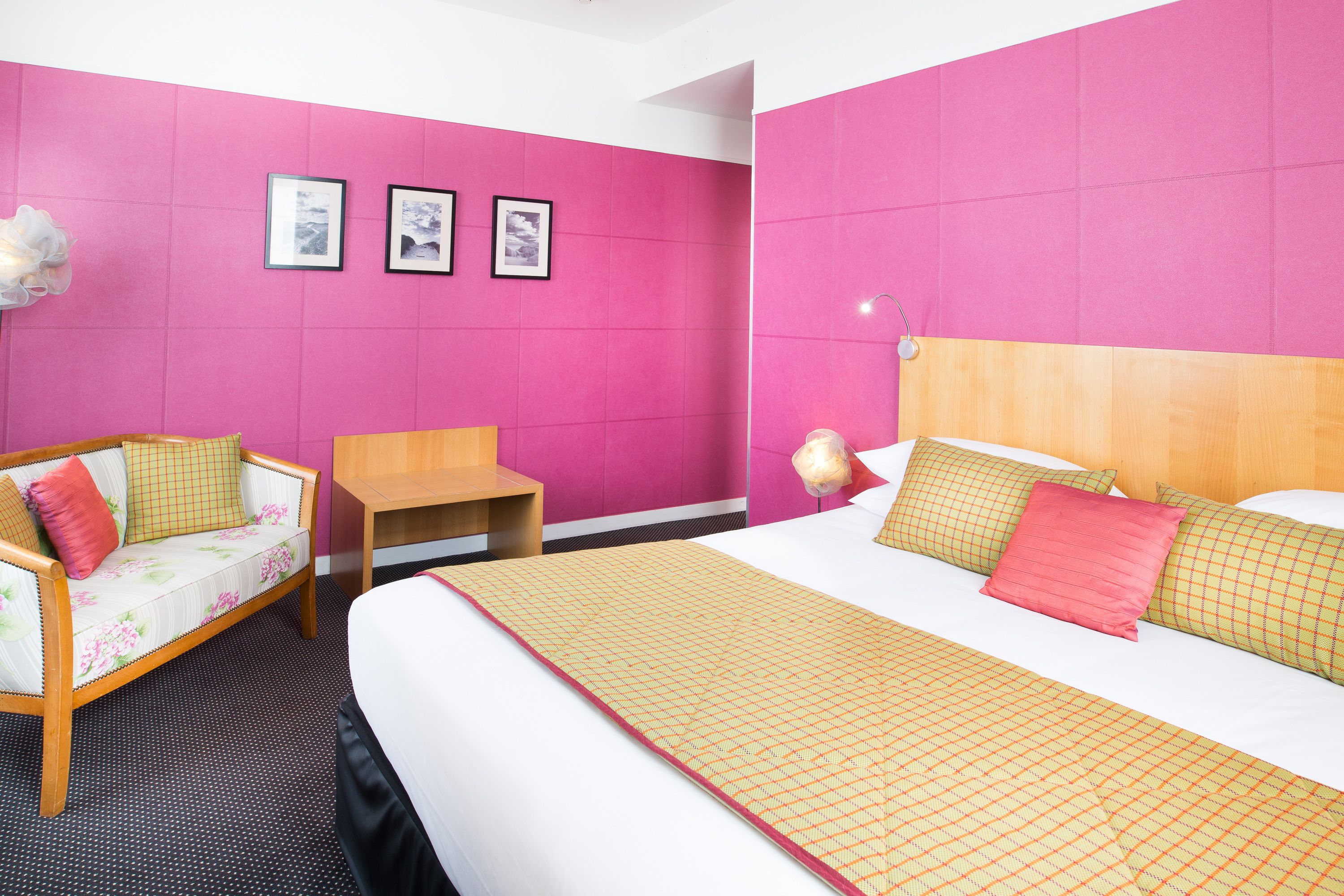 A hotel room with a bed, a sofa, a small table, and three framed pictures on the wall.
