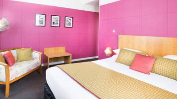 A hotel room with a bed, a sofa, a small table, and three framed pictures on the wall.