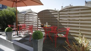 An outdoor patio with red chairs and a table, a large umbrella, and a wooden fence. - Best Western Adagio (Saumur)