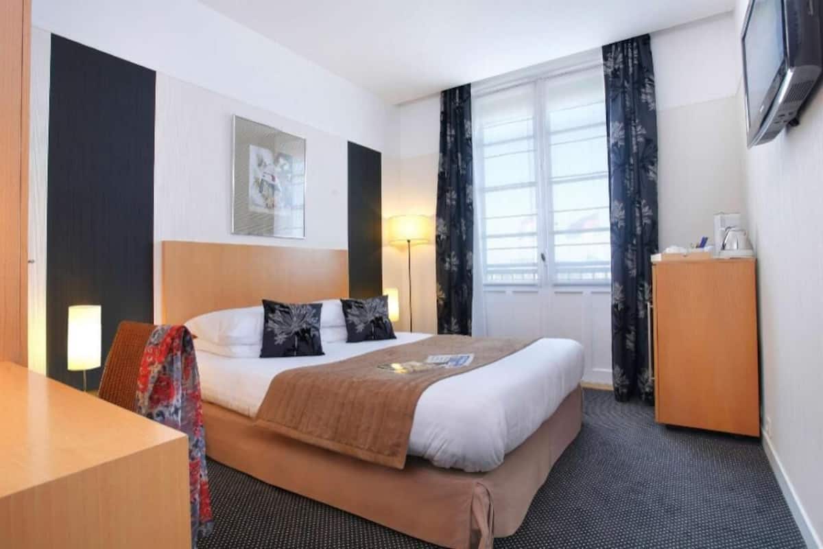 A hotel room with a bed, bedside table, lamp, and a television.