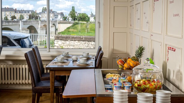 A breakfast setup with a view of a bridge and buildings, a buffet with fruits and dairy products, and a dining area with chairs and a table. - Best Western Adagio (Saumur)