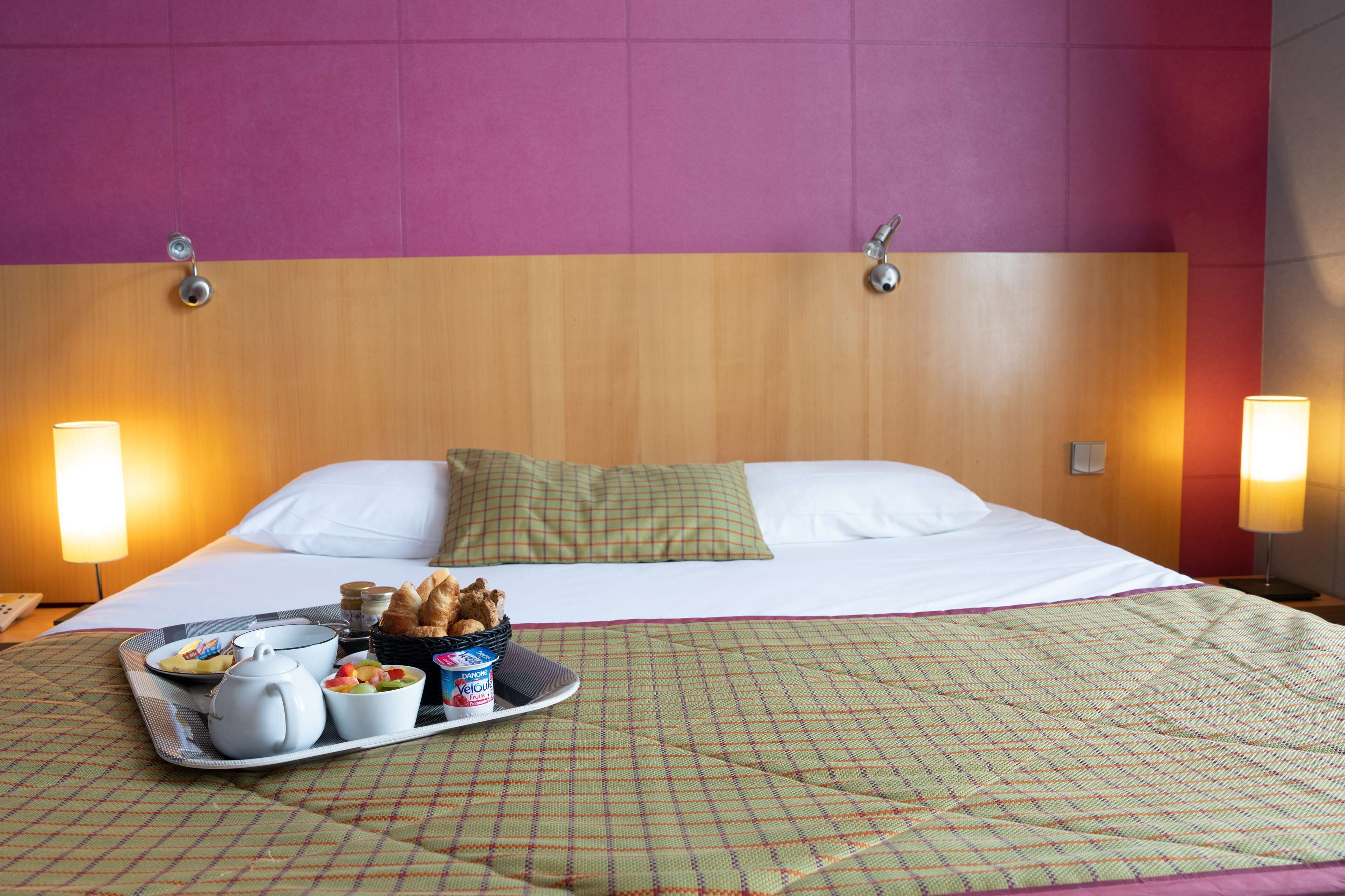 A hotel room with a bed, pillows, a tray with breakfast items, and bedside lamps.