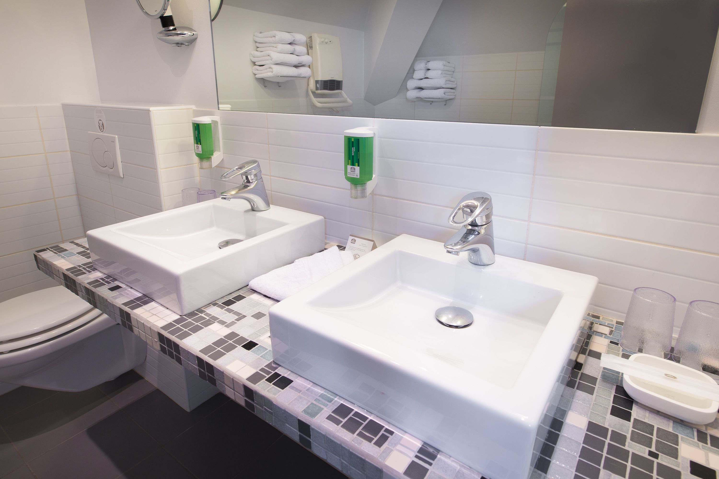 A bathroom with two sinks, a toilet, and a mirror.
