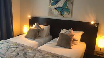 A double bed with a patterned bedspread, two pillows, a headboard, wall-mounted lights, and a butterfly painting.