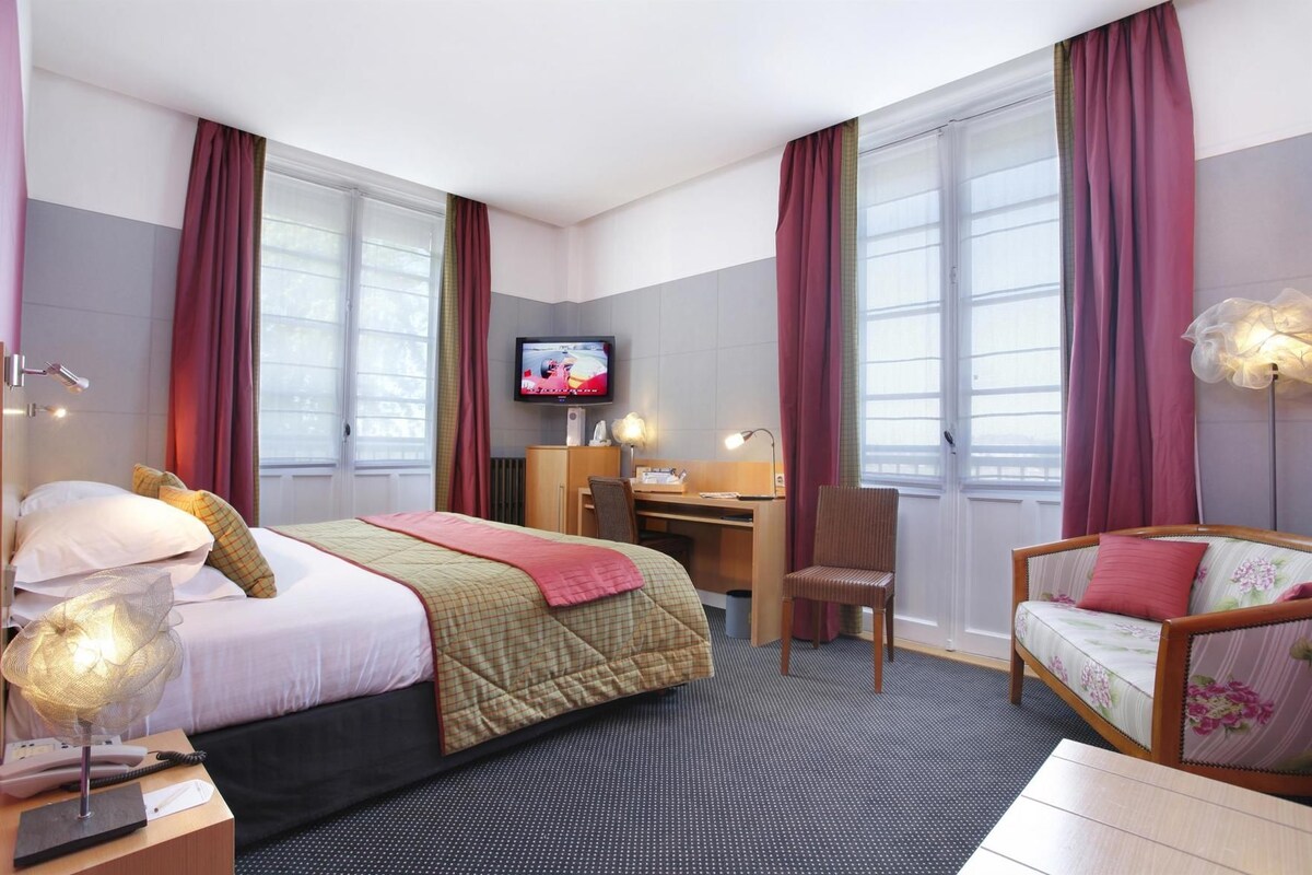 A hotel room with a bed, desk, chair, television, and a sofa.