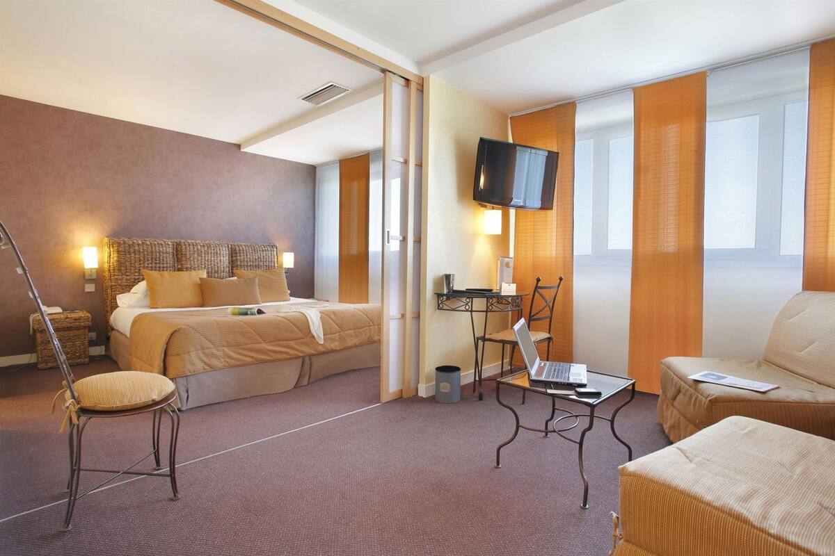 A hotel room with a bed, a desk with a laptop, a TV, and a sofa.
