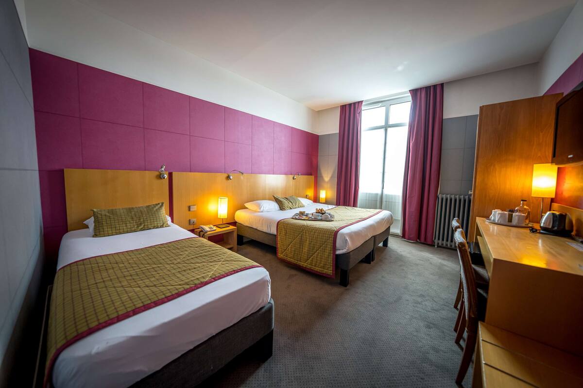 A hotel room with two beds, a desk, and a window with curtains.