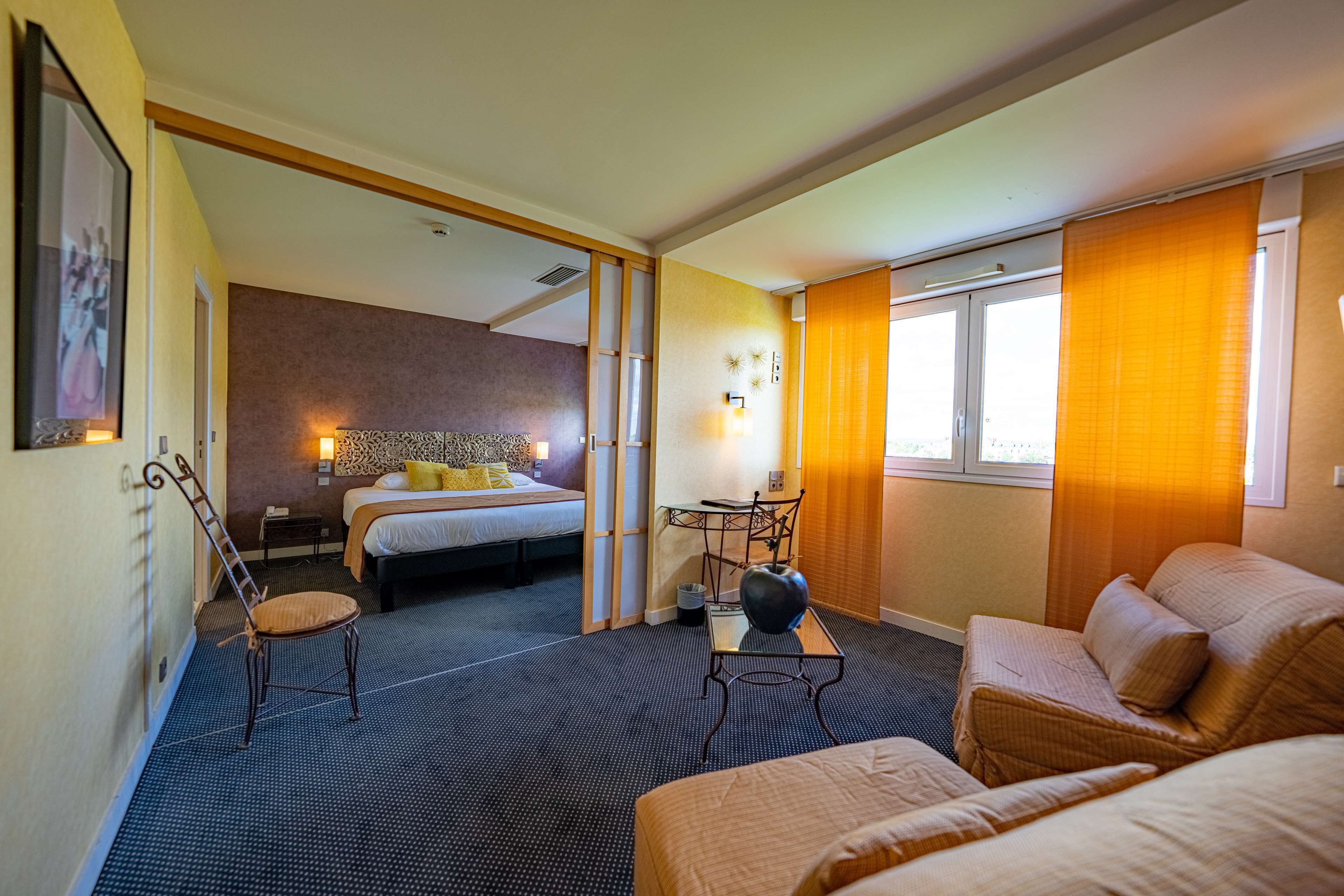 A hotel room with a bed, a desk, a chair, and a sofa.