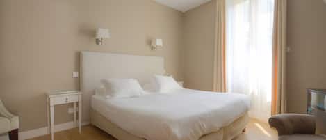 A bedroom with a large bed, a nightstand, a chair, and a window with curtains.