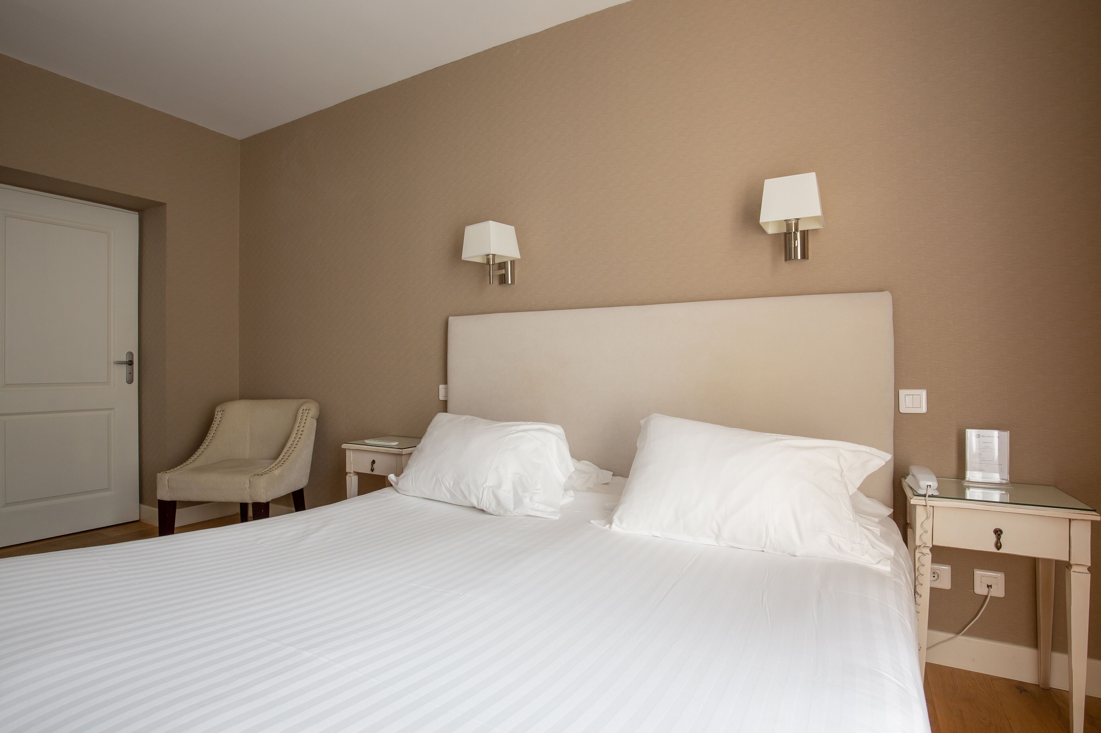 A hotel room with a large bed, two bedside tables, a chair, and two wall-mounted lamps.