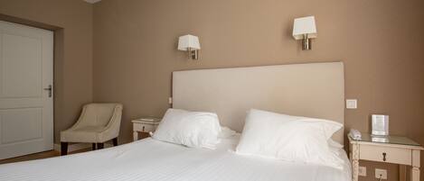 Una habitación de hotel con una cama grande, dos mesitas de noche, una silla y dos lámparas de pared.