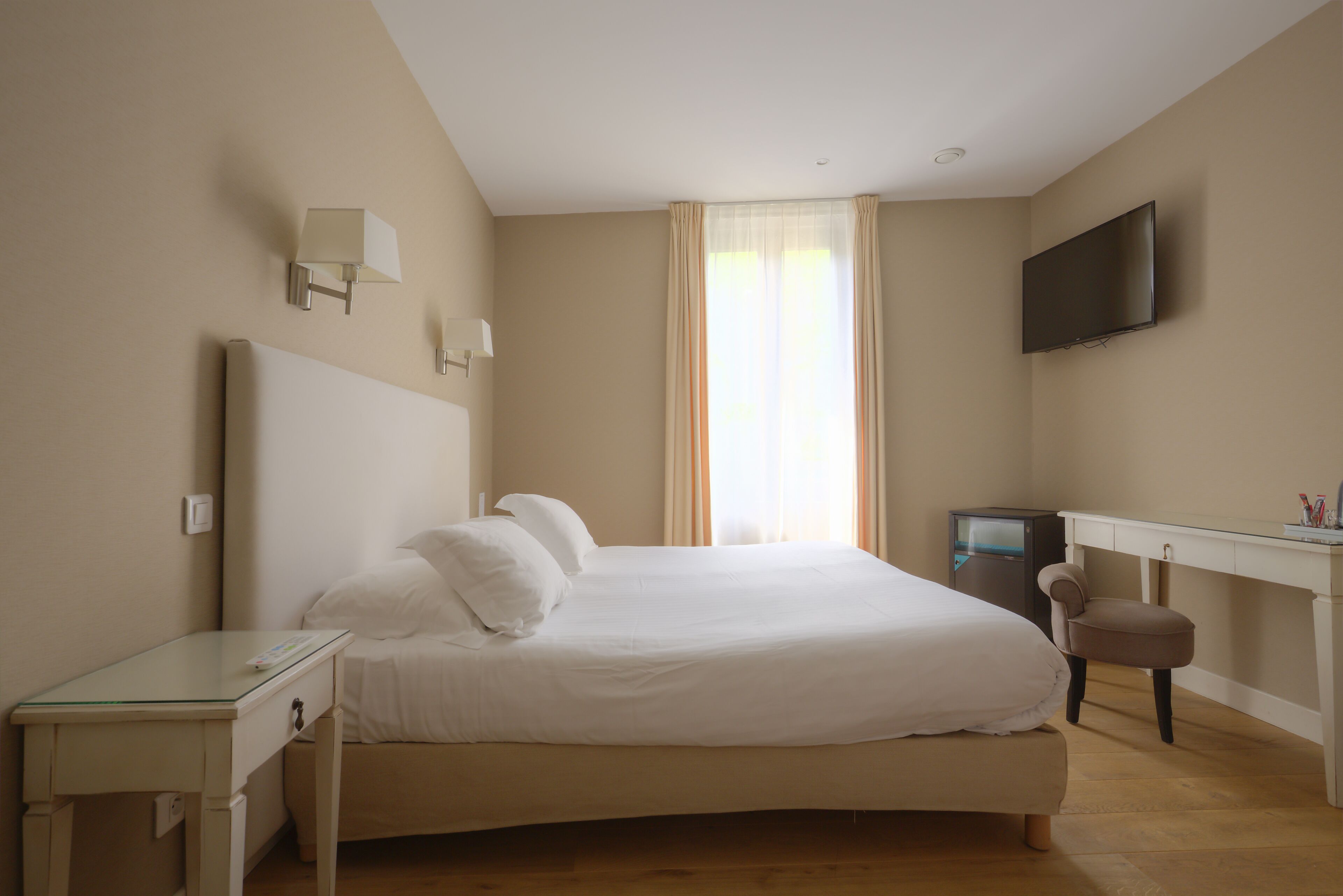 A bedroom with a bed, bedside table, desk, chair, TV, and curtains.