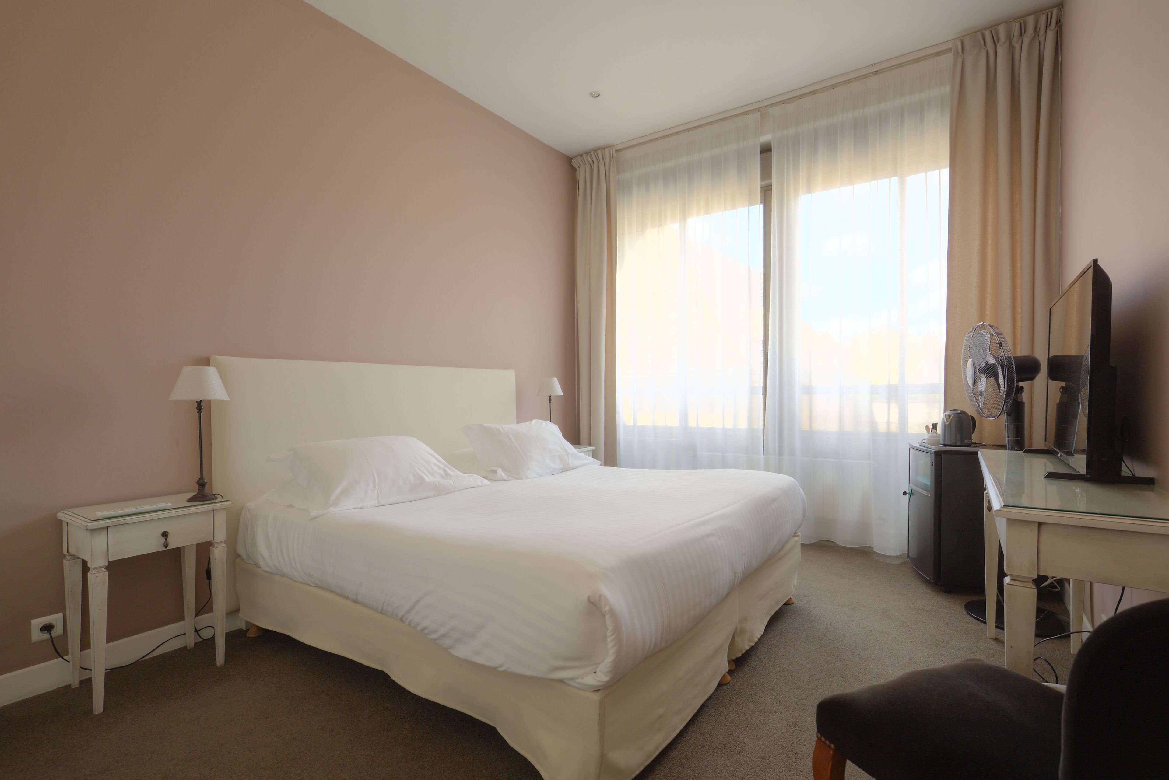 Habitación de hotel con una cama grande, un escritorio con computadora, una silla y una ventana con cortinas.