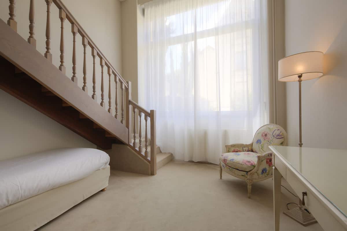 Een slaapkamer met een houten trap, een fauteuil met bloemenprint, een nachtkastje en een lamp.