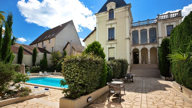 A courtyard with a swimming pool, outdoor seating, and a large building with a balcony. - Hotel Le Renoir (Sarlat-la-Canéda)