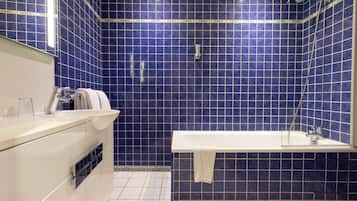 A bathroom with blue tiles, a white bathtub, and a white sink with a towel hanging on it.