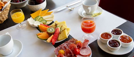 Un bufé de desayuno con diversas frutas, quesos, embutidos y bebidas.