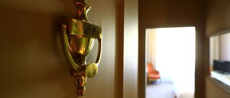 A brass doorbell with the number 27 on a hallway wall.