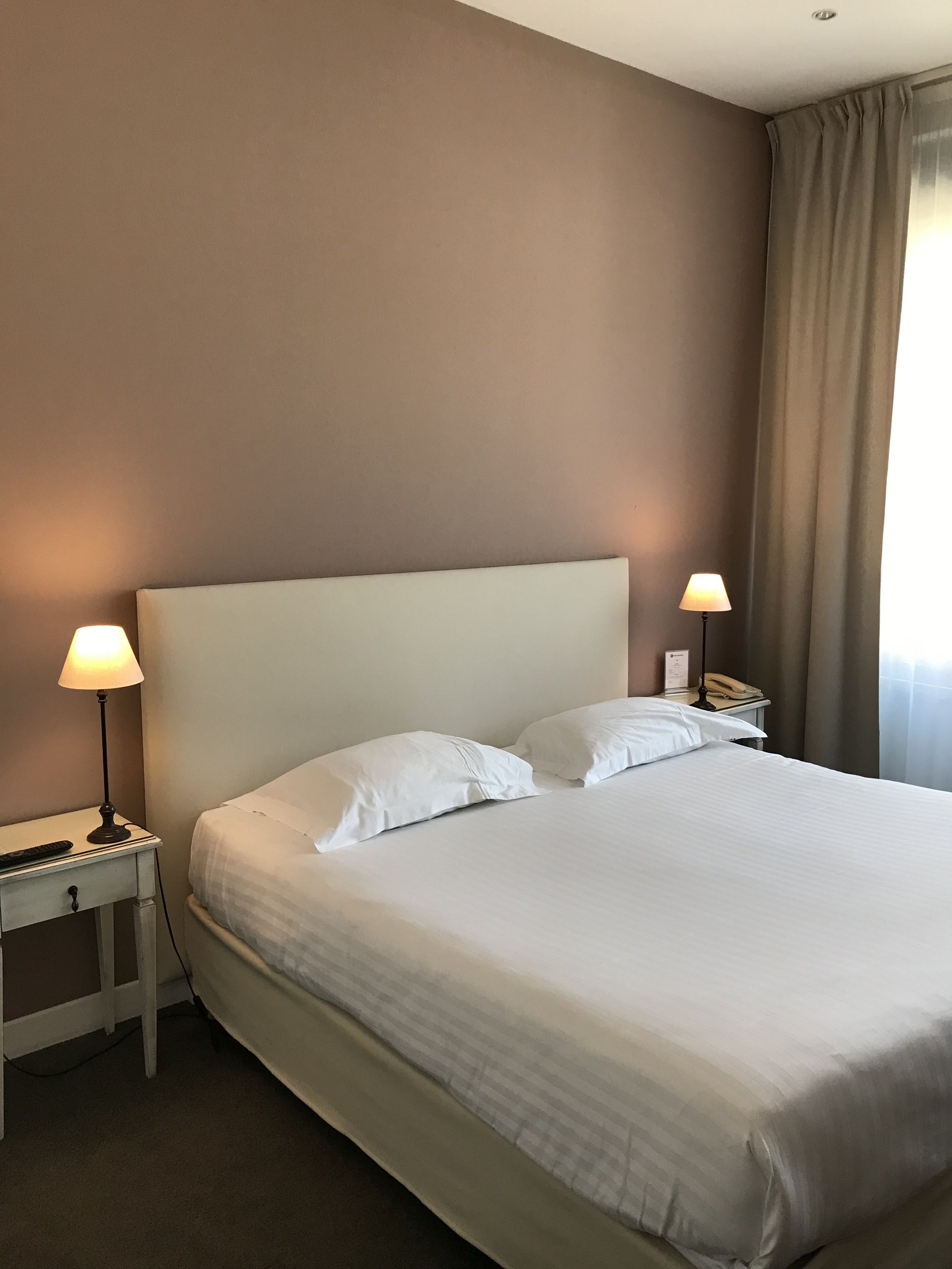 Ein ordentlich bezogenes Bett mit weißen Leinentüchern, zwei Nachttischlampen und ein Telefon auf dem Nachttisch.
