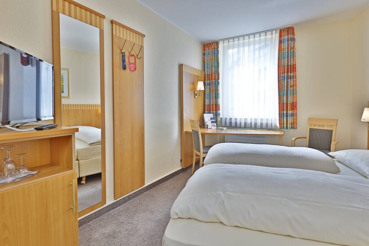 Habitación de hotel con cama, escritorio, silla, espejo y televisor.