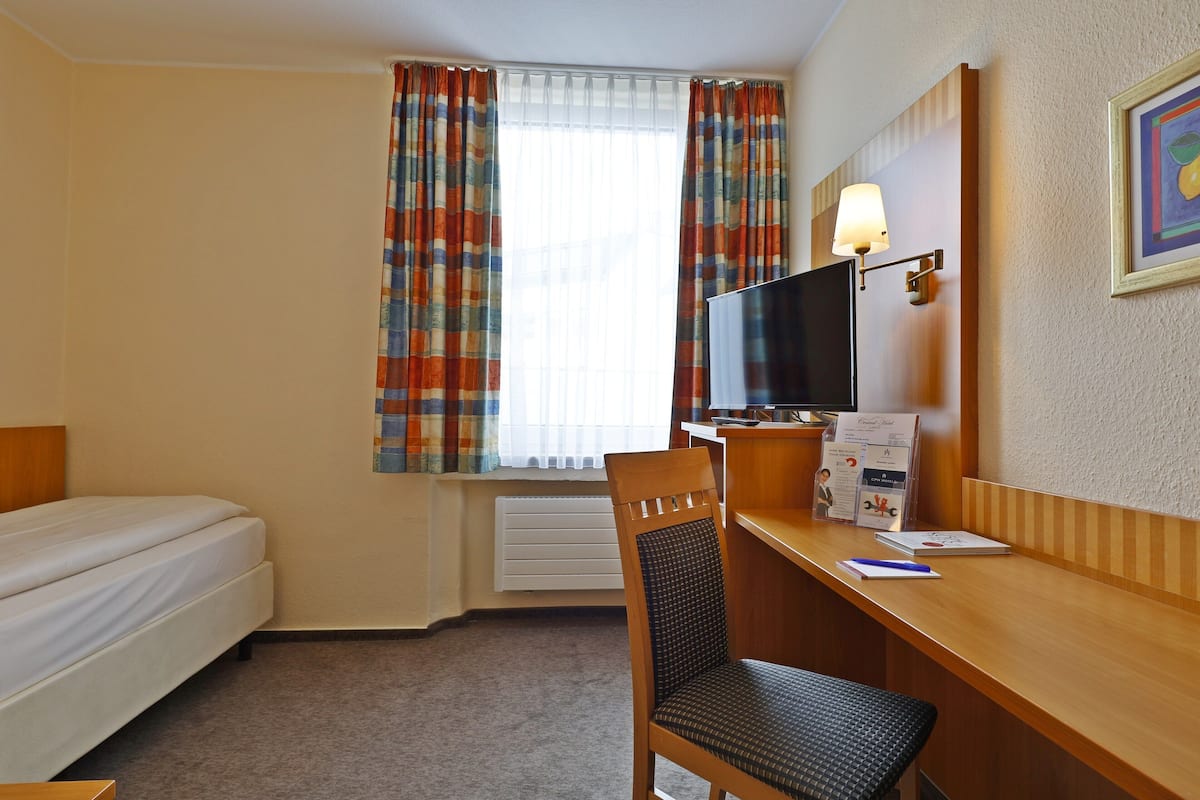 Habitación de hotel con una cama, un escritorio con ordenador, una silla y una ventana con cortinas.