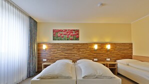 Ett hotellrum med två sängar, en sänggavel i trä, en tavla med röda blommor som hänger på väggen och två sänglampor.