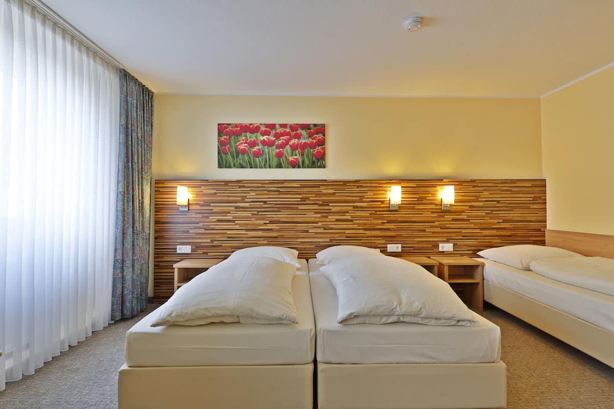 Habitación de hotel con dos camas, cabecero de madera, un cuadro con flores rojas colgado en la pared y dos lámparas de noche.