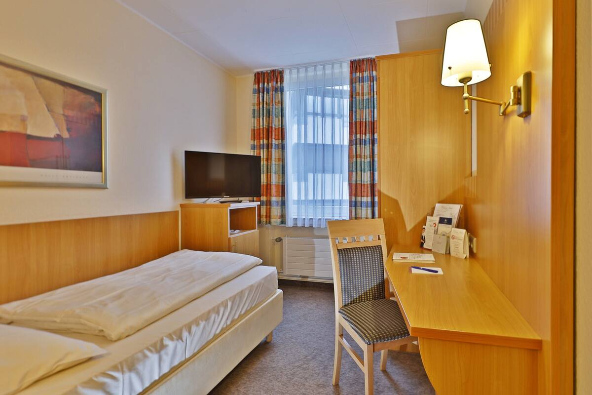Una habitación de hotel con una cama, un escritorio con silla, un televisor y una ventana con cortinas.