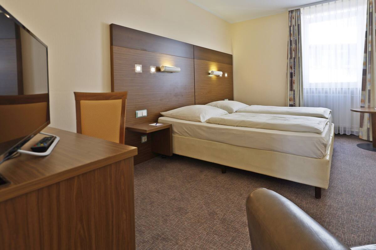 Una habitación de hotel con una cama, un escritorio con teléfono, una silla y una mesita de noche.