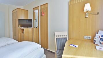 A hotel room with a bed, a desk with a lamp, a chair, and a TV.