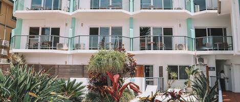 Un hotel de varios pisos con balcones, piscina y diversas plantas.
