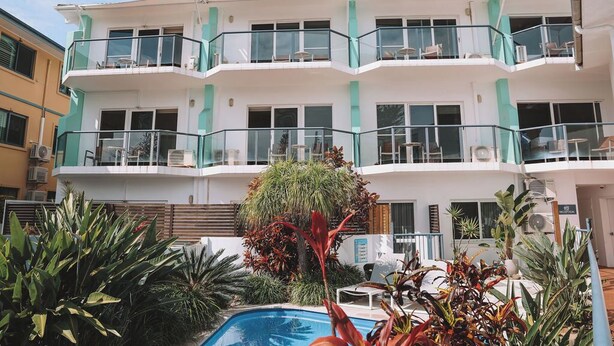 A multi-story hotel with balconies, a swimming pool, and tropical plants.