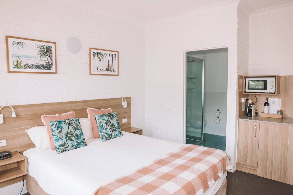 A hotel room with a bed, a wooden headboard, a microwave, a nightstand, and a wall with two framed pictures.