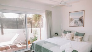 A bedroom with a bed, a ceiling fan, a window with a view of the outdoors, and a painting on the wall.