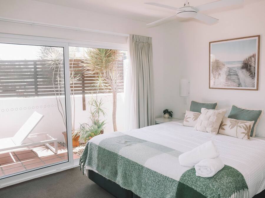 Un dormitorio con cama, ventilador de techo, ventana con vistas al exterior y un cuadro en la pared.