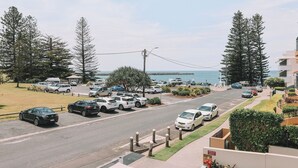 A street view with parked cars, a road, and a body of water in the distance.