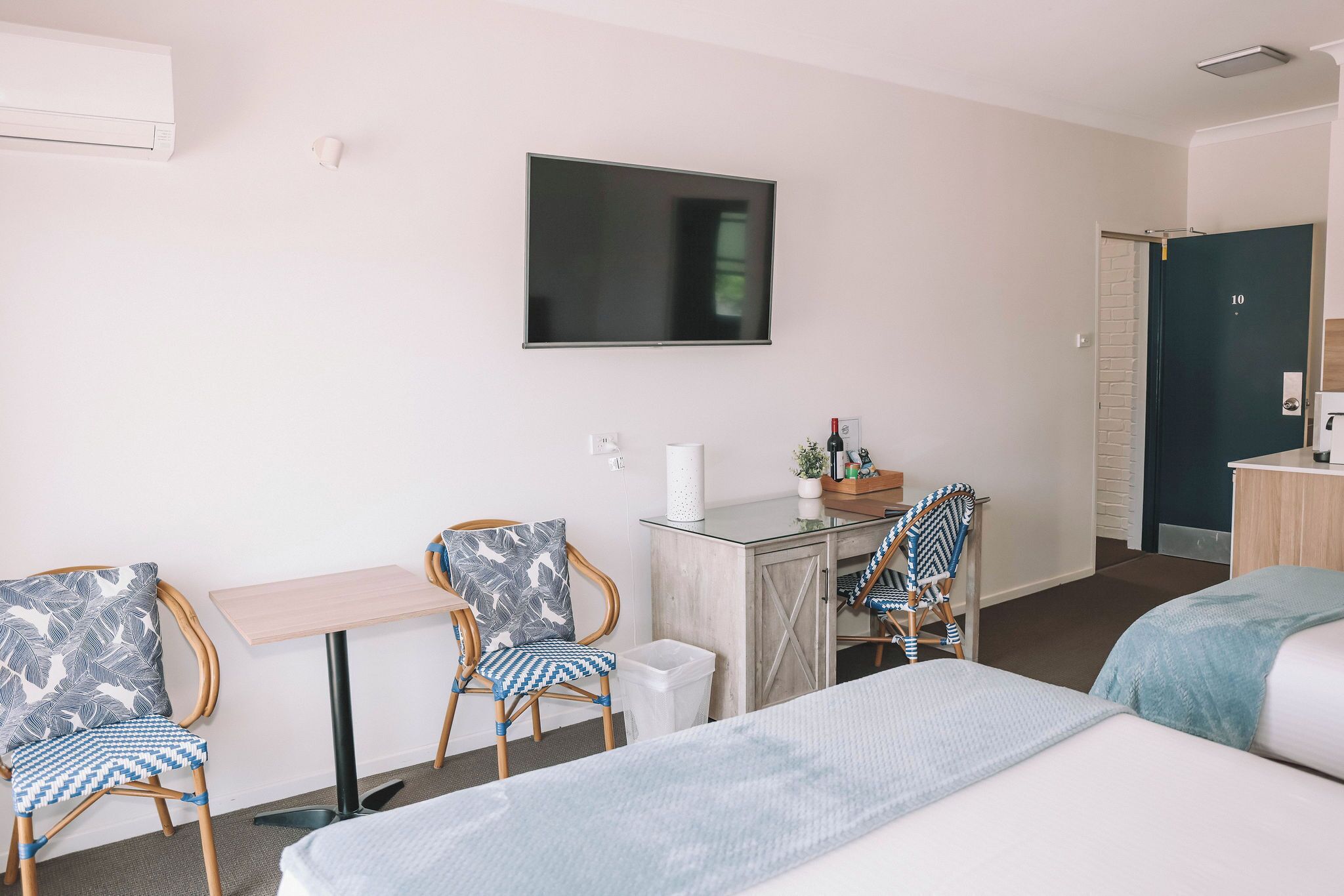 Hotellihuone, jossa on sänky, kaksi tuolia, pieni pöytä, televisio ja ovi.
