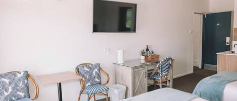 Hotellihuone, jossa on sänky, kaksi tuolia, pieni pöytä, televisio ja ovi.