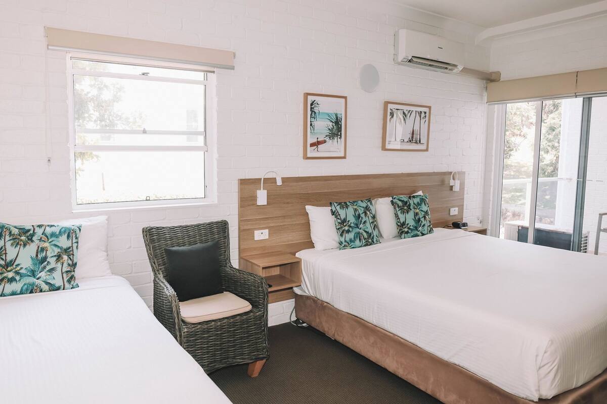 A hotel room with a large bed, a chair, a wooden headboard, and two framed pictures on the wall.
