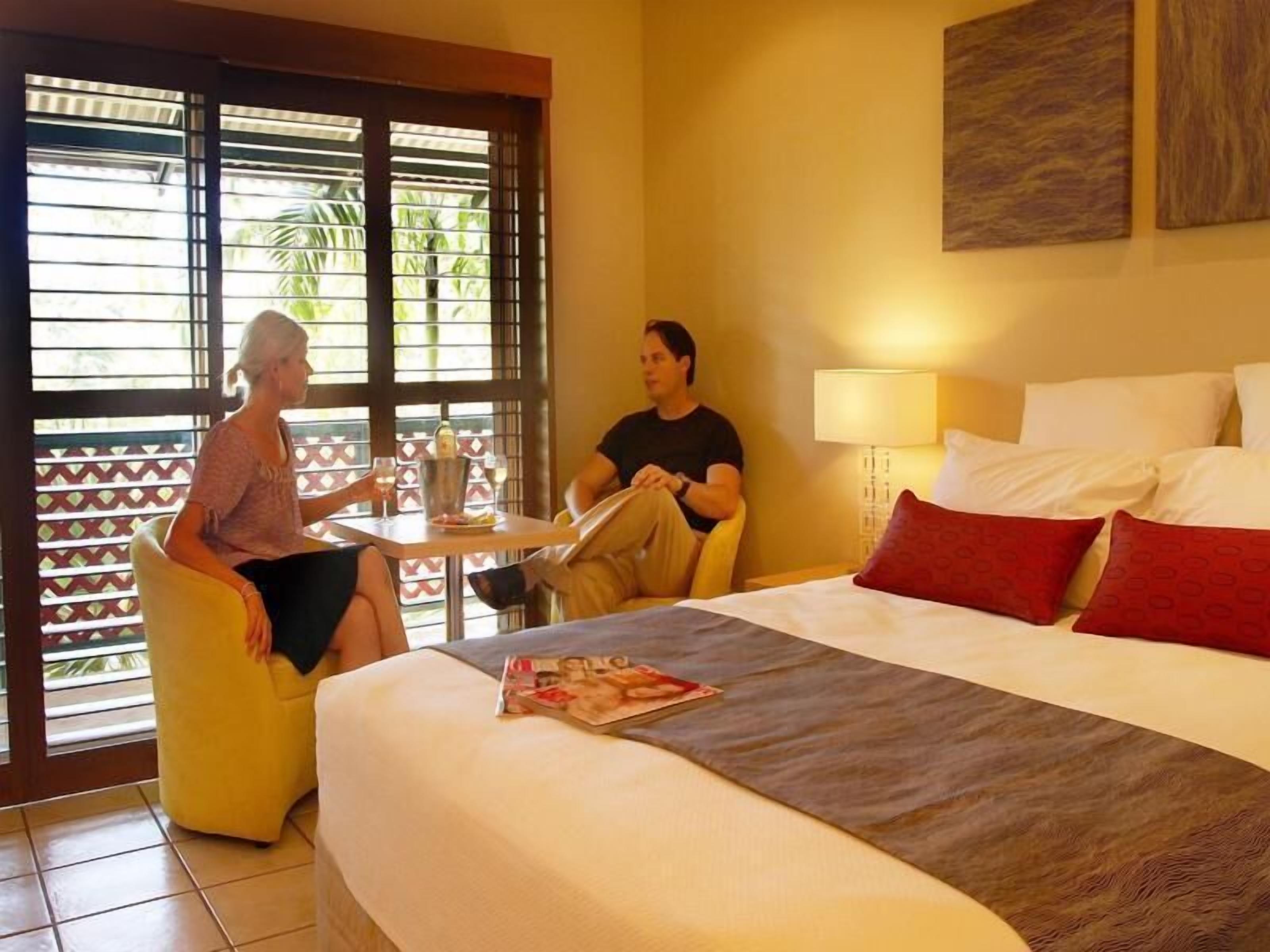 A hotel room with a bed, a table with drinks, and a window with blinds.