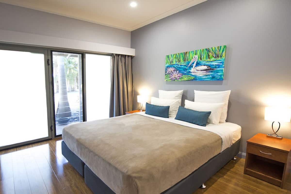 Une chambre d’hôtel moderne avec un grand lit, un tableau représentant un oiseau et une vue à travers la porte-fenêtre coulissante.