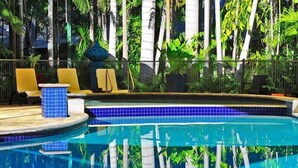 Una piscina con azulejos azules, rodeada de palmeras y sillas de descanso.
