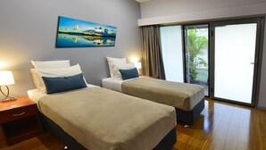 Habitación de hotel con dos camas, un cuadro en la pared, una mesita de noche y un ventanal corredizo al exterior.