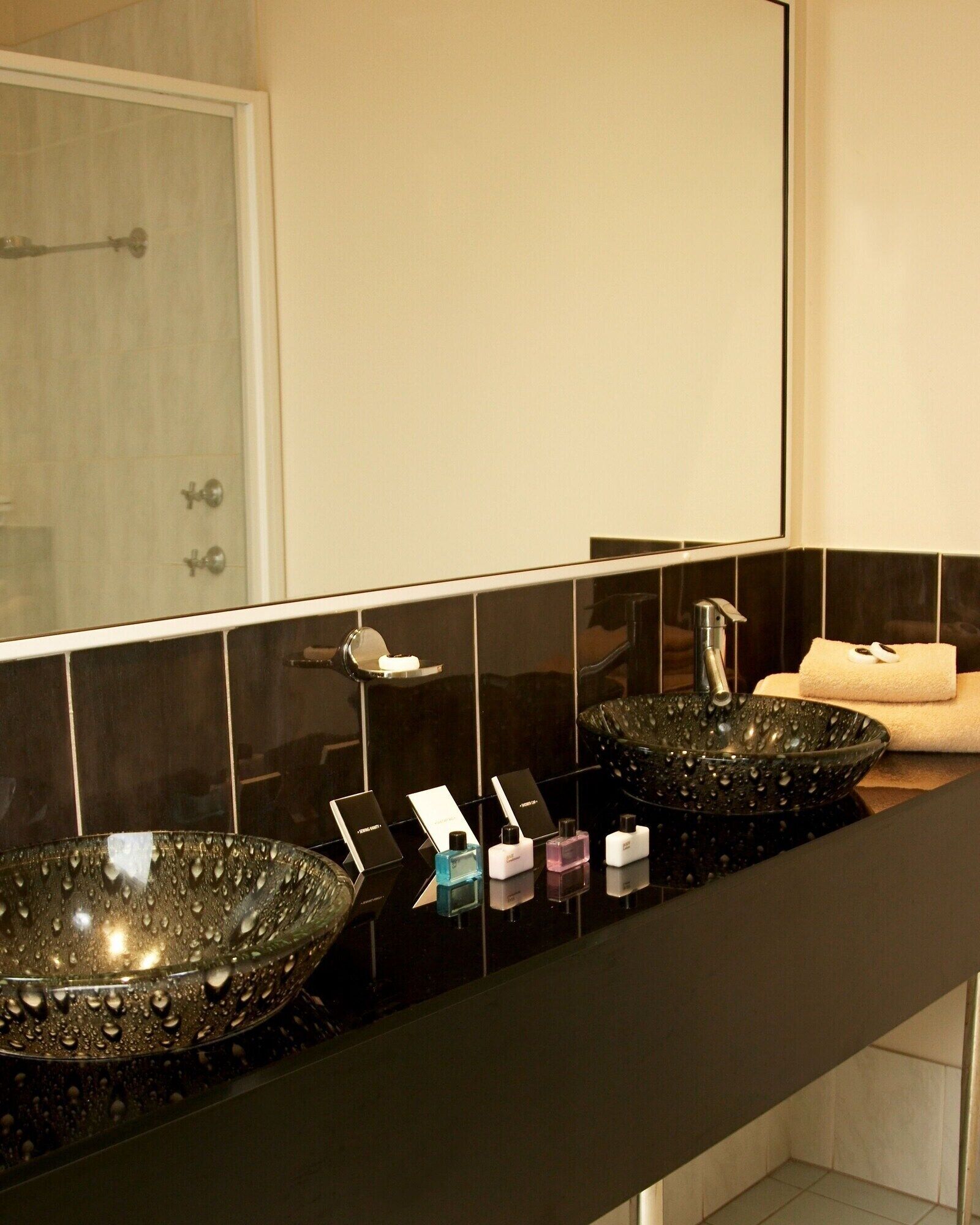 A modern bathroom with two large glass sinks, a mirror, and a towel rack.