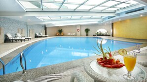 An indoor swimming pool with a glass ceiling, lounge chairs, and a table with a drink and fruit. - Central Hotel Jingmin (Xiamen)