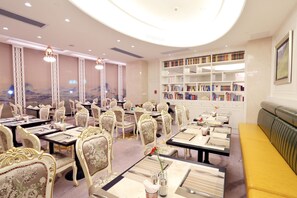 A dining area with tables set for service, ornate chairs, and a bookshelf filled with books. - Central Hotel Jingmin (Xiamen)
