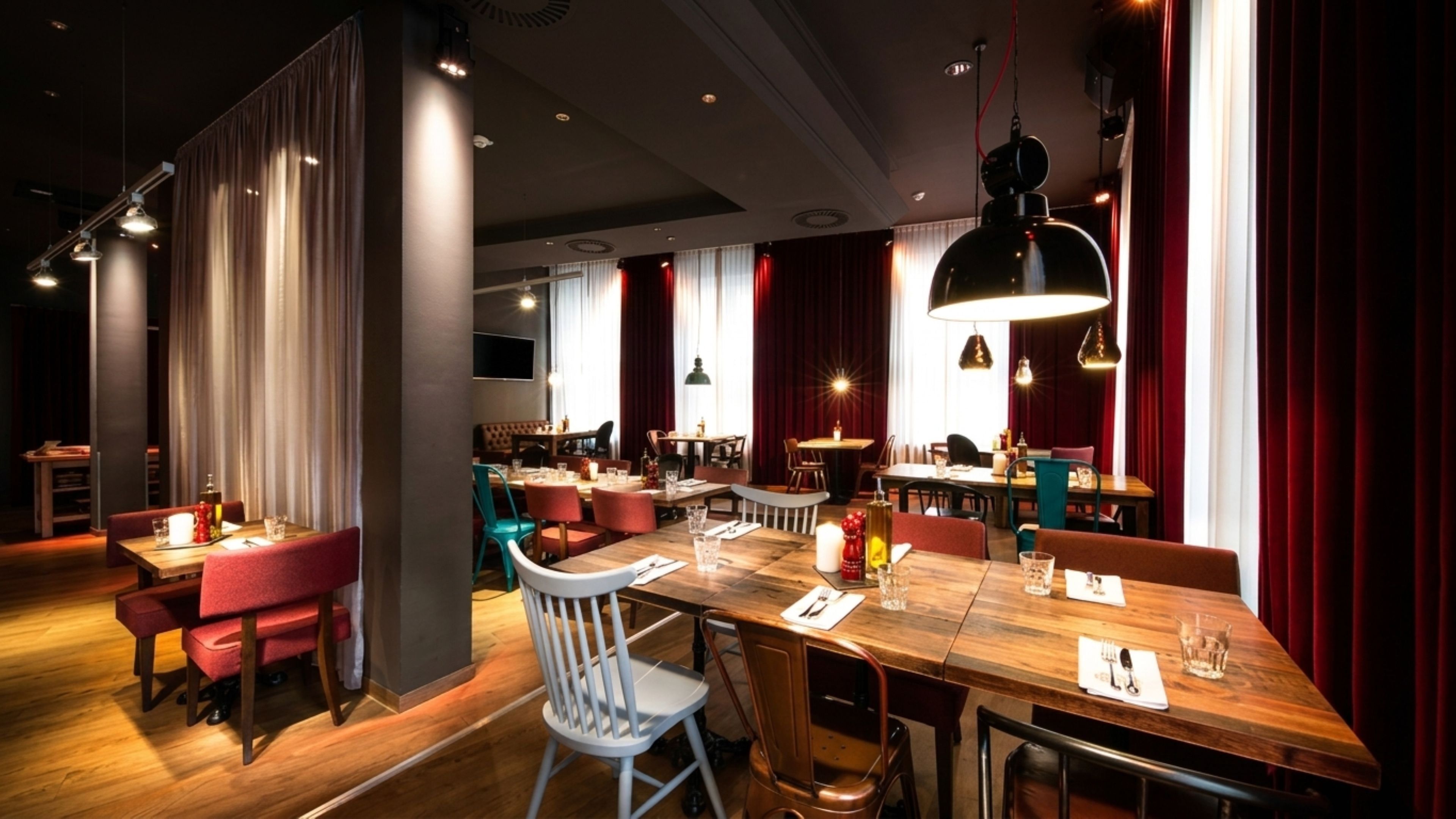 L’intérieur d’un restaurant avec des tables en bois, des chaises rouges et blanches, et des luminaires suspendus.