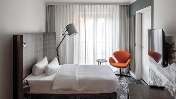 A hotel room with a bed, a desk, a chair, a lamp, and a large mirror. - Pentahotel Braunschweig (Braunschweig)