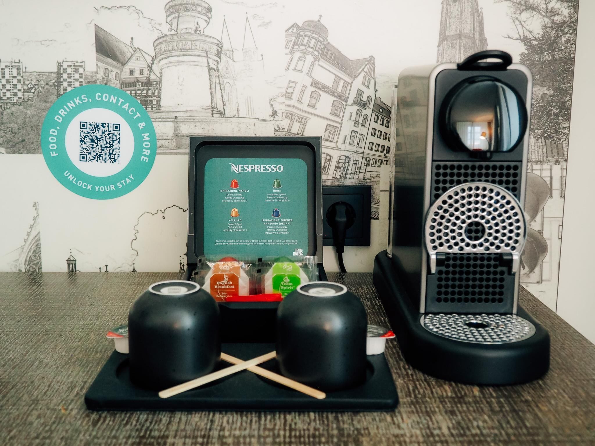 Una macchina per caffè Nespresso con erogatore manuale per cialde espresso, due tazzine da caffè e un codice QR per cibo, bevande e contatti.