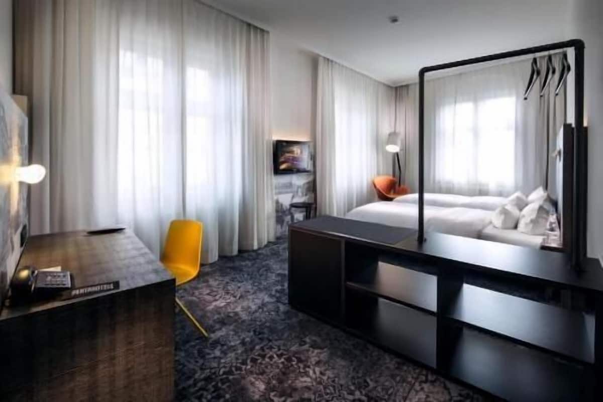 Una habitación de hotel con cama, escritorio, silla, espejo grande y televisor.